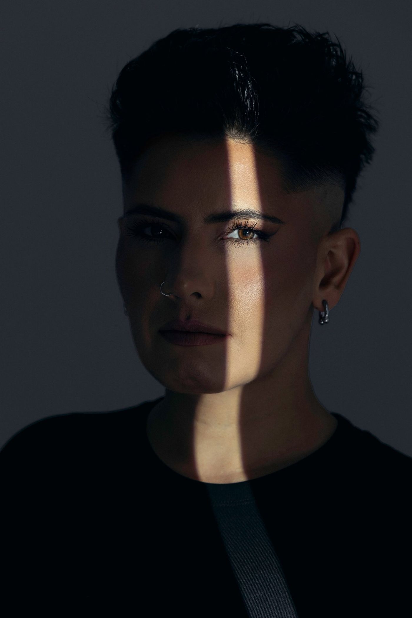 Portrait of Chris 73, a beam of light across her face in a dark room